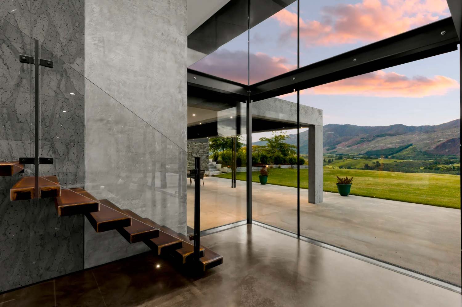 Modern house interior with glass sliding doors open to a lawn and mountains sunset sky